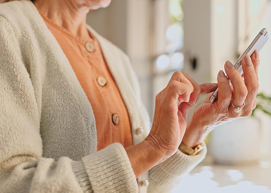 Older woman wearing a peach sweater texting on her phone — PeopleImages // Shutterstock