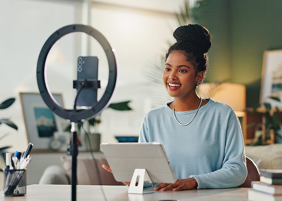 A young woman filming vlog content at home using her smartphone and a tripod. — PeopleImages // Shutterstock