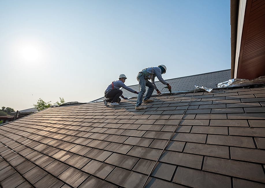 Two roof workers in full gear as they replace tiling on a roof. — Tong_stocker // Shutterstock