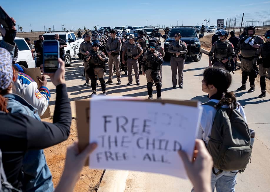 Texas State Troopers surrounded by protesters as they denounce detention of 5-year-old, Liam Ramos, at an immigration processing facility in Texas. One person holding a 'free the child, free all' sign put it up facing the troopers. — Joel Angel Juarez // Getty Images