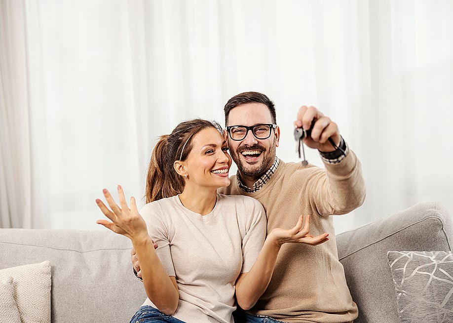 A happy couple taking a photo and showing off their new home's keys to the camera. — Dusan Petkovic // Shutterstock
