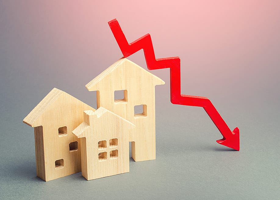 Figures of wooden homes and a red declining arrow as a concept of decline in real estate. — Andrii Yalanskyi // Shutterstock