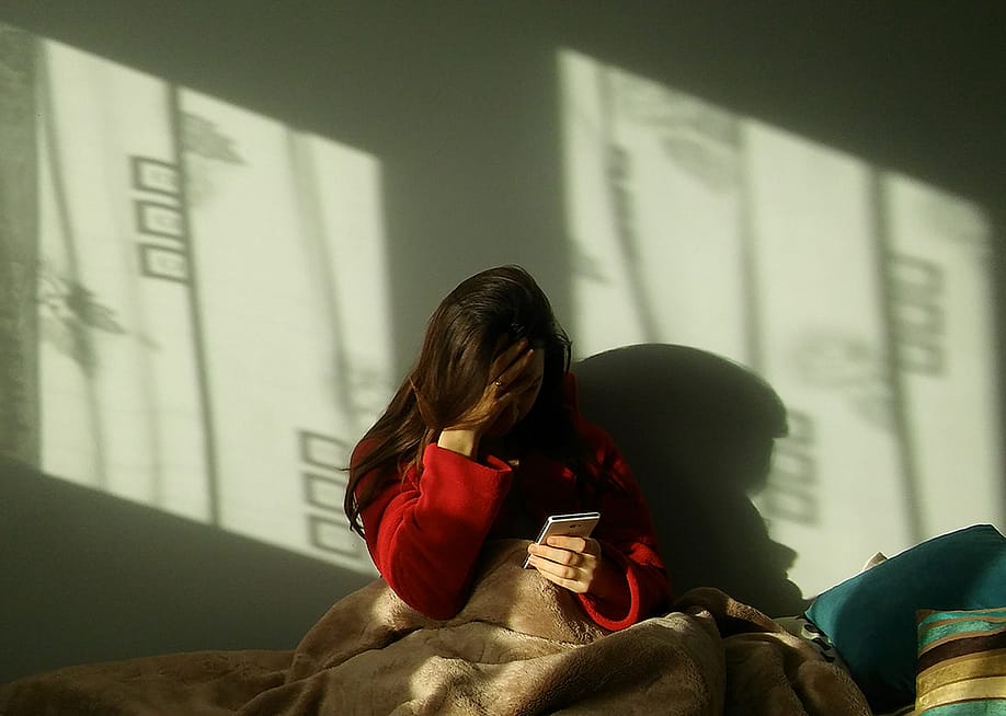 A sad woman in bed making a call on her phone. — Andrzej Wilusz // Shutterstock