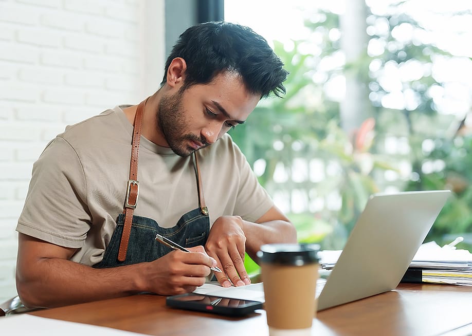 A young small cafe business owner reviewing reports at a cafe desk. — Ekkasit A Siam // Shutterstock