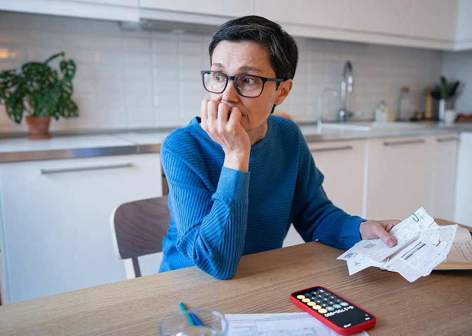 A stressed middle-aged woman looking away from bills at home. — DimaBerlin // Shutterstock