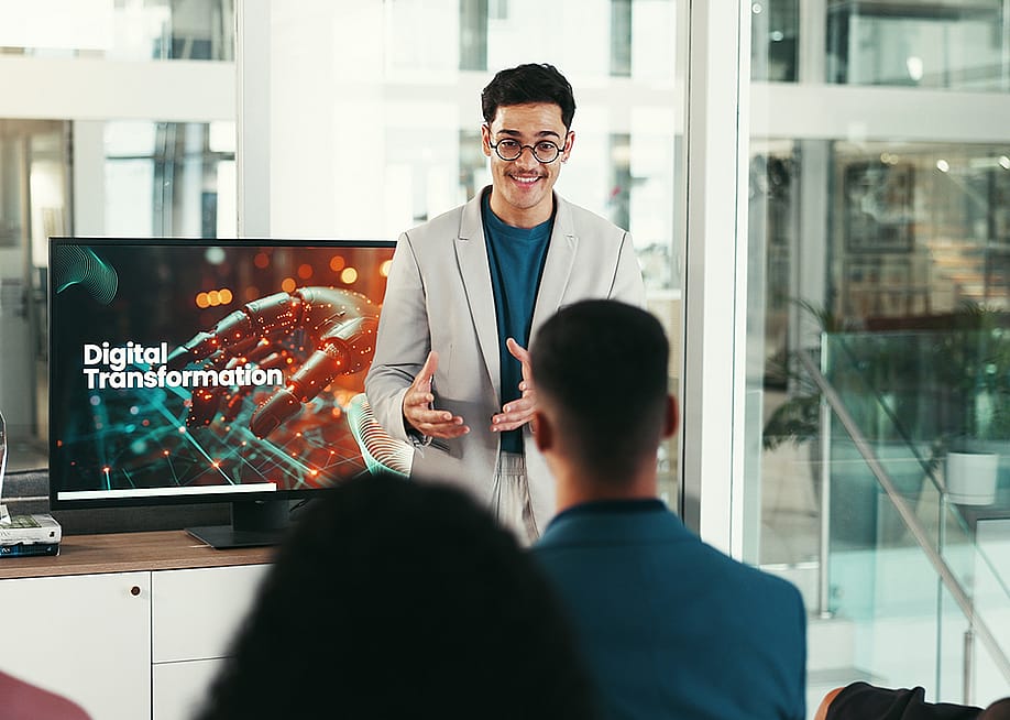 A young male public speaker giving a talk about digital transformation to a group of corporate employees at a conference. — PeopleImages // Shutterstock