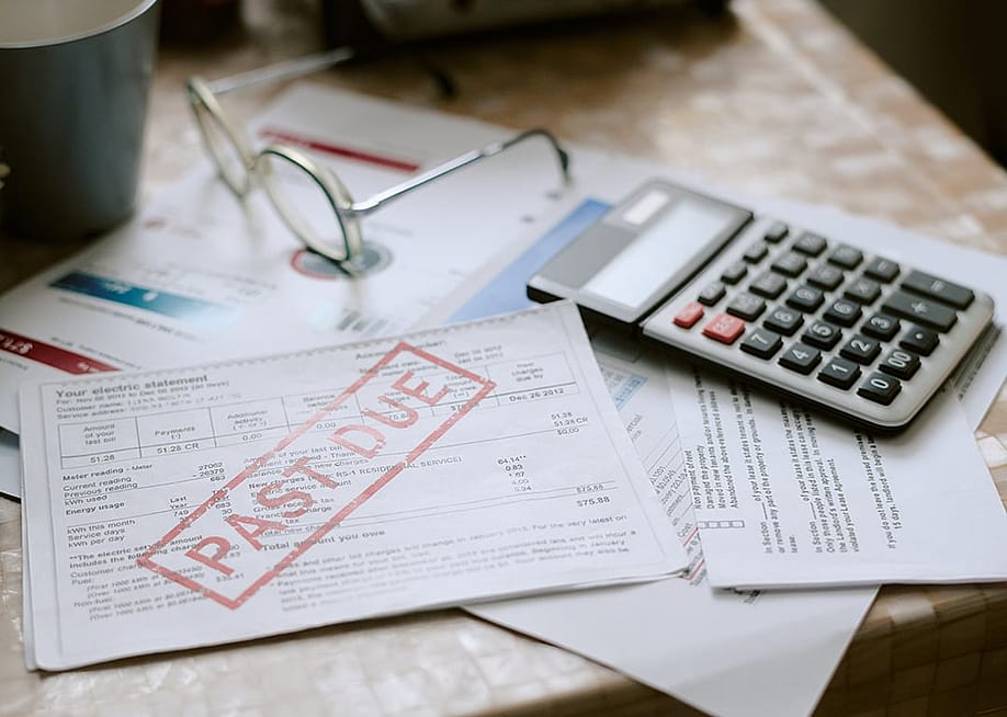 Bills stamped with a past due sign beside a calculator on top of a desk. — AnnaStills // Shutterstock