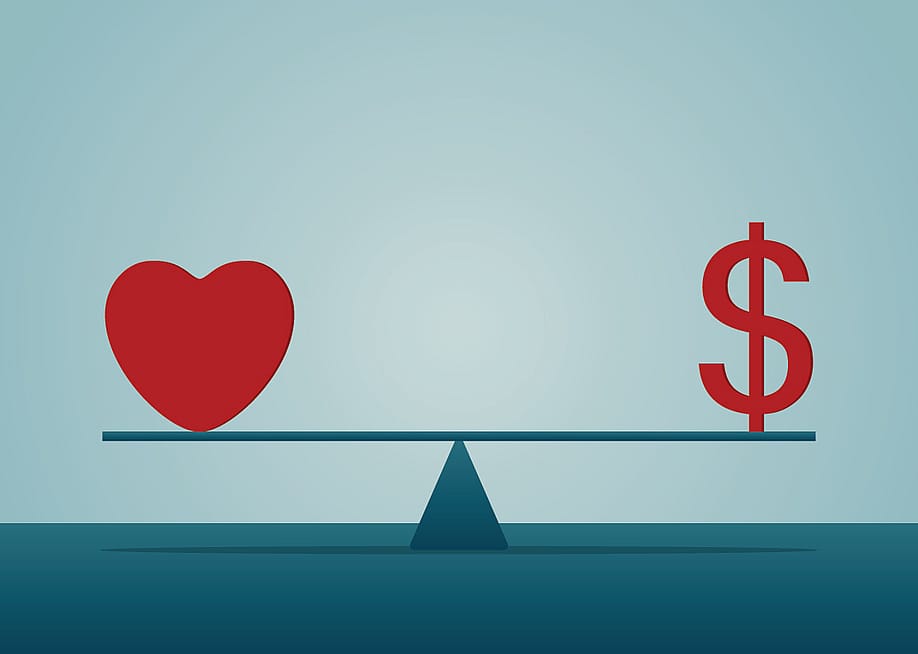 A heart and a dollar symbol on both ends of a seesaw. — Champ008 // Shutterstock