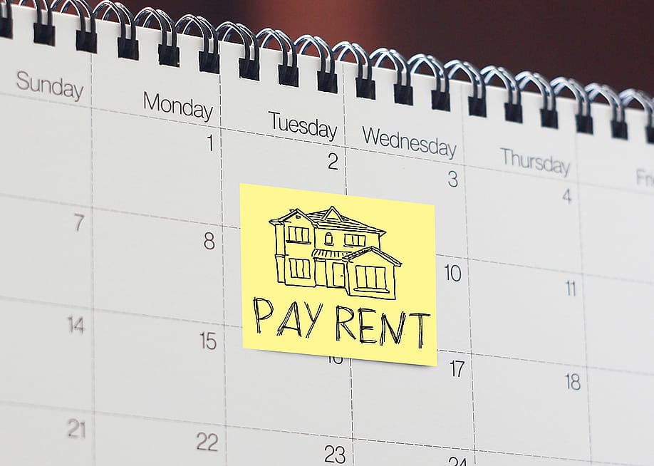 A note written with 'pay rent' as a reminder stuck onto a calendar. — Jack_the_sparow // Shutterstock