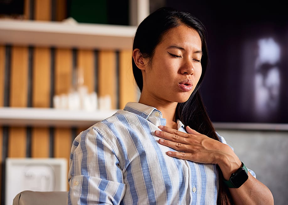 A young woman with her hand on her chest, practicing a breathing technique at home. — Branislav Nenin // Shutterstock