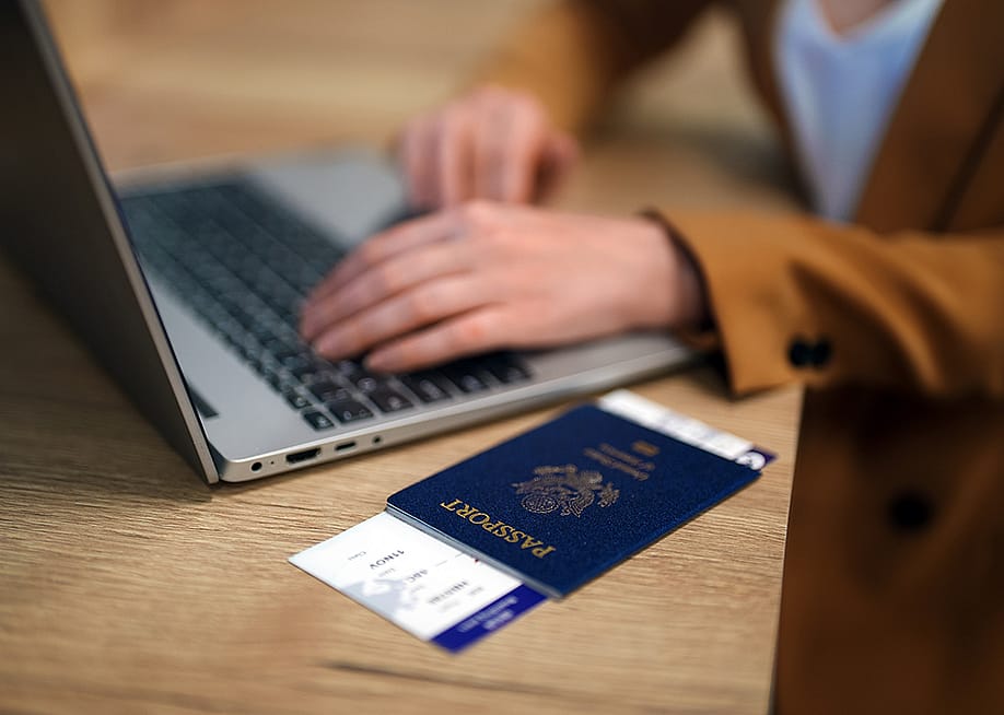 Female traveler using laptop with passport ready at the side while waiting for her flight. — M-Production // Shutterstock.