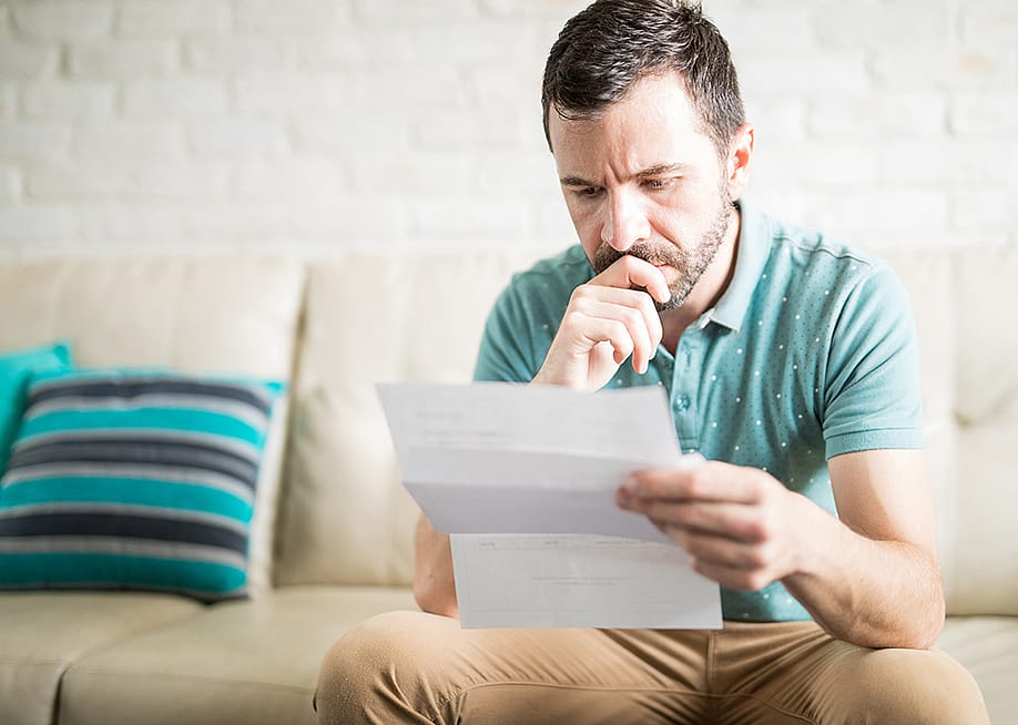 A man at home pensively looking at a debt document. — antoniodiaz // Shutterstock
