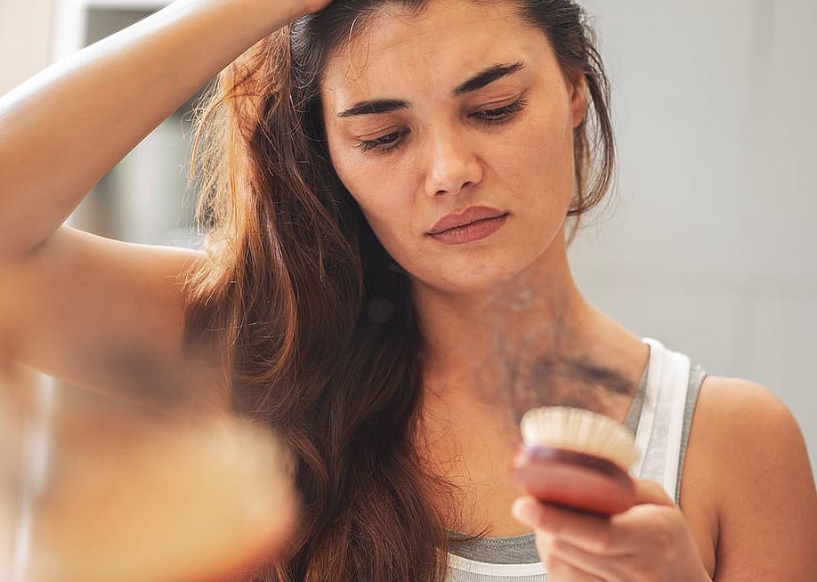 A woman staring at hair loss accumulated in her hairbrush. — sebra // Shutterstock