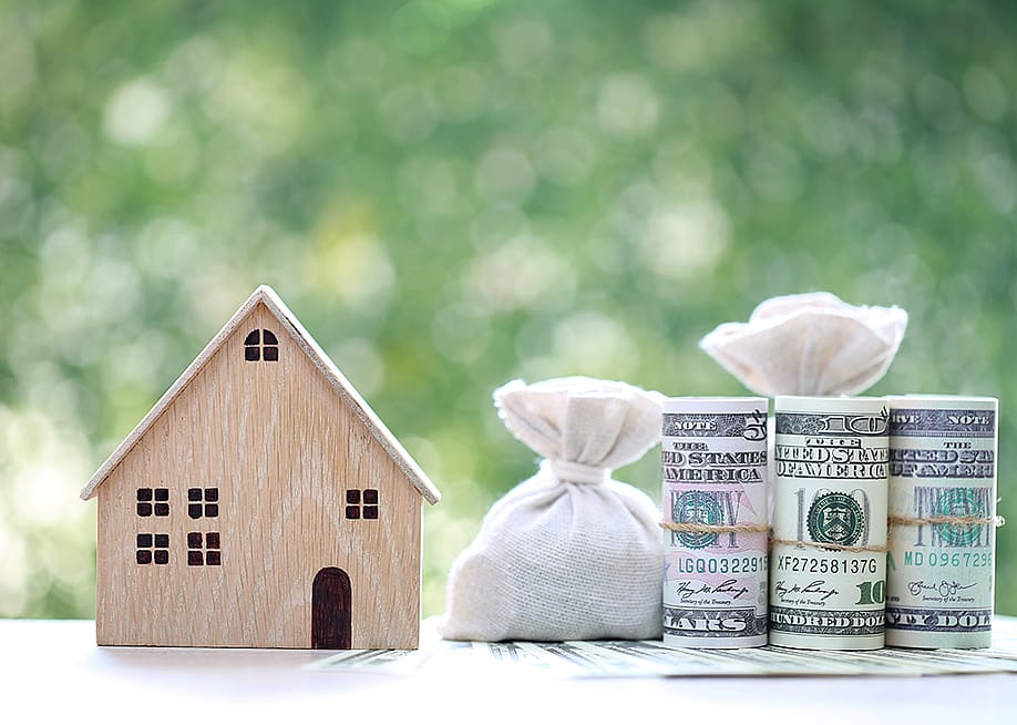 A wooden figure of a model house with banknotes on the side as a concept of saving money for a home. — Monthira // Shutterstock
