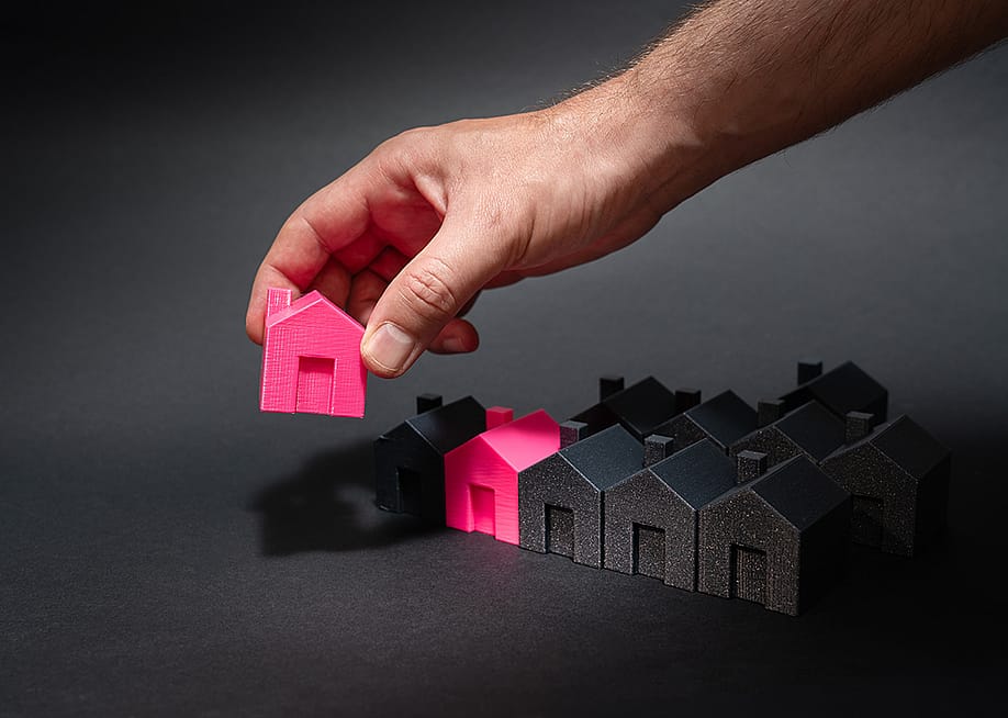 Figures of pink model houses being lined up with a row of black houses as a concept of national housing supply. — Jakub Zerdzicki // Shutterstock