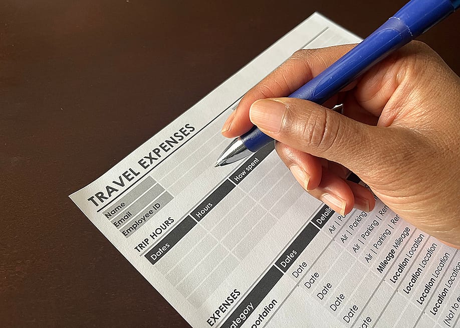 Person completing a travel expense form. — Jenari // Shutterstock