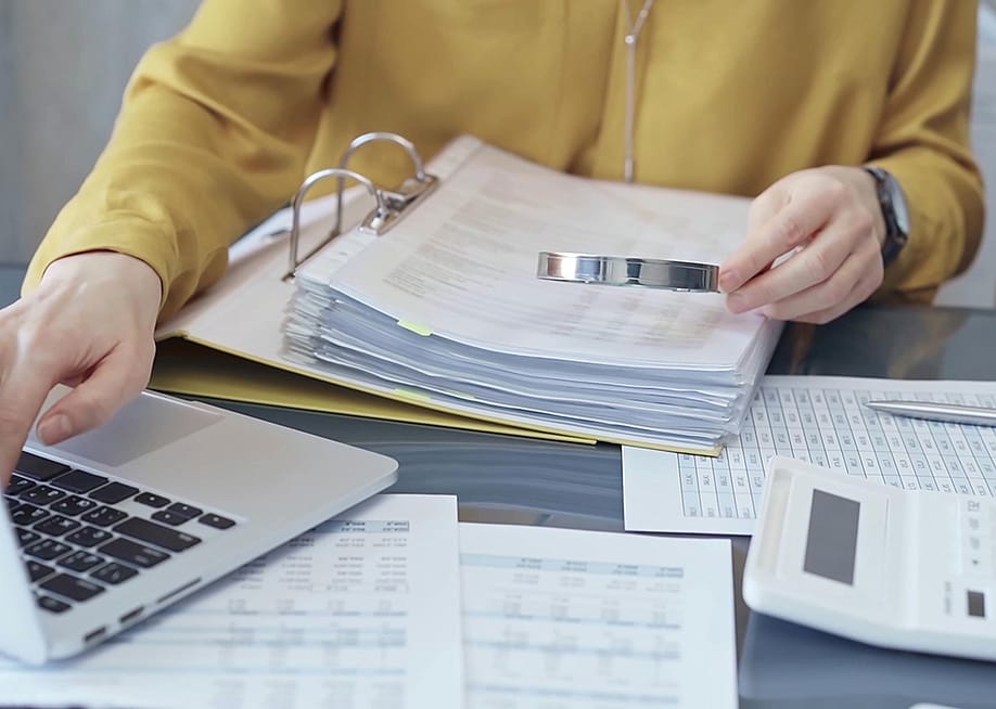 An auditor reviewing financial reports using a magnifying glass. — Volha_R // Shutterstock
