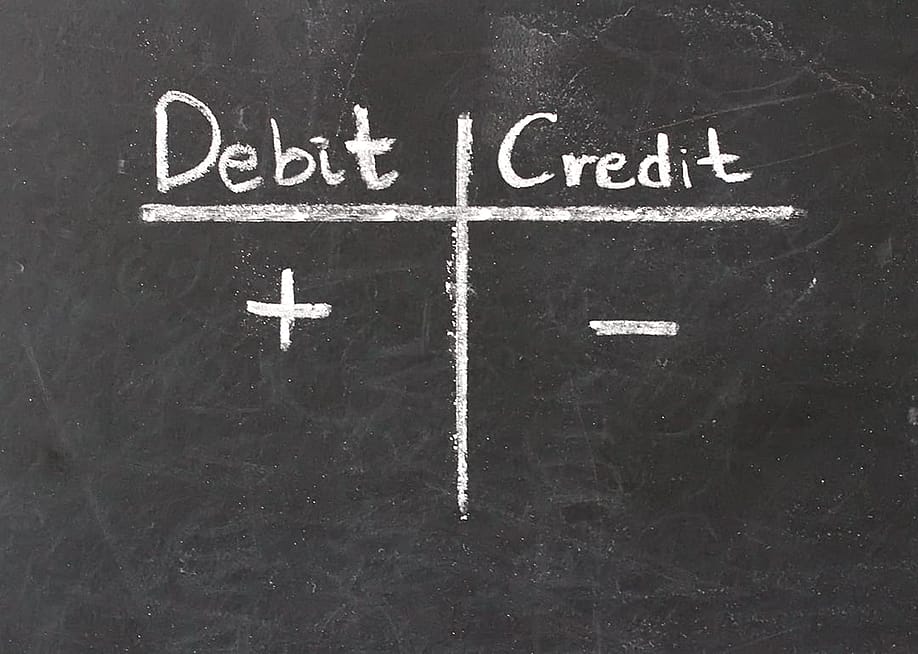 A chalkboard with 'Debit' and 'Credit' written in a table with plus and minus symbols. — jensanny // Shutterstock