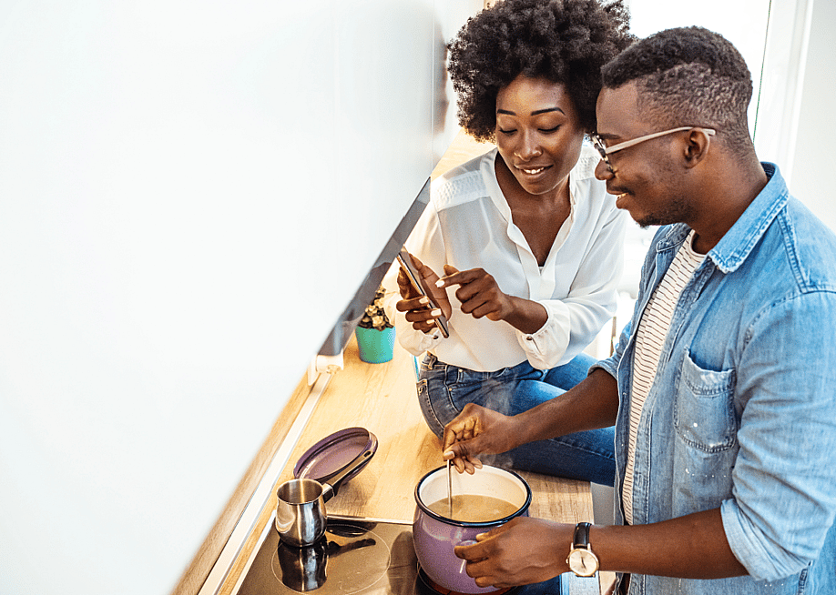 Young couple is using a smartphone and smiling while cooking in kitchen at home. — Dragana Gordic // Shutterstock