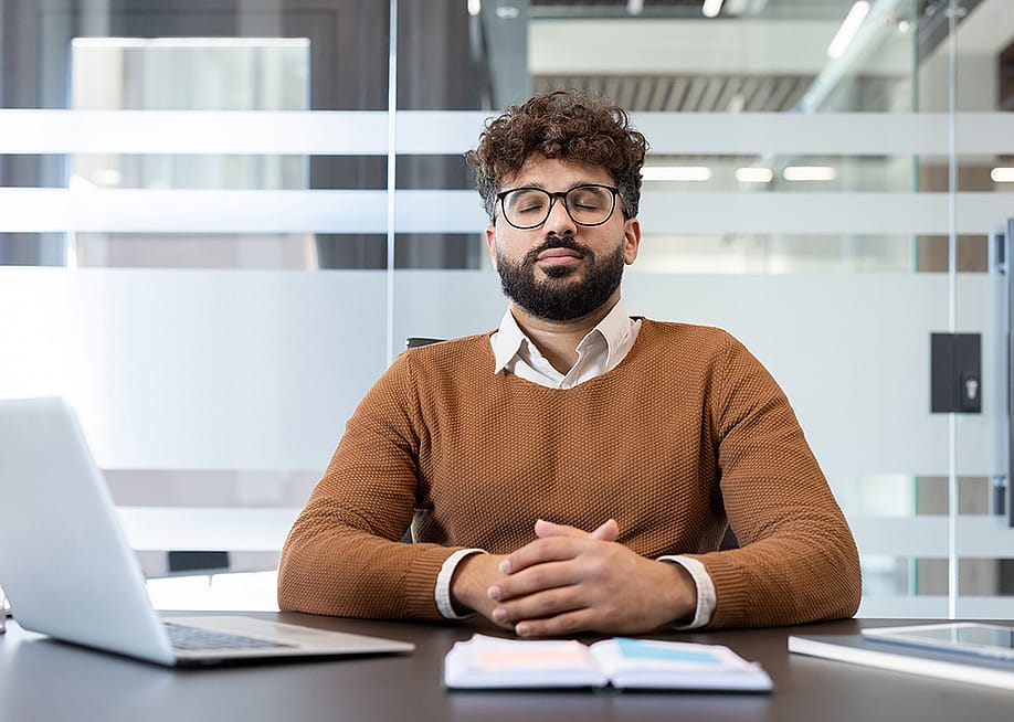 A man with eyes closed meditating at his office desk. — voronaman // Shutterstock