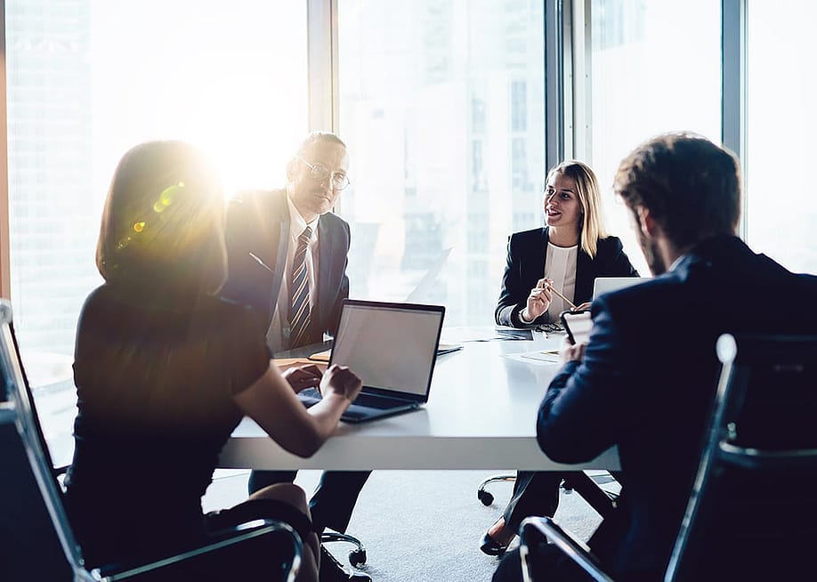 Businesspeople gathered at a roundtable in an office meeting room. — GaudiLab // Shutterstock