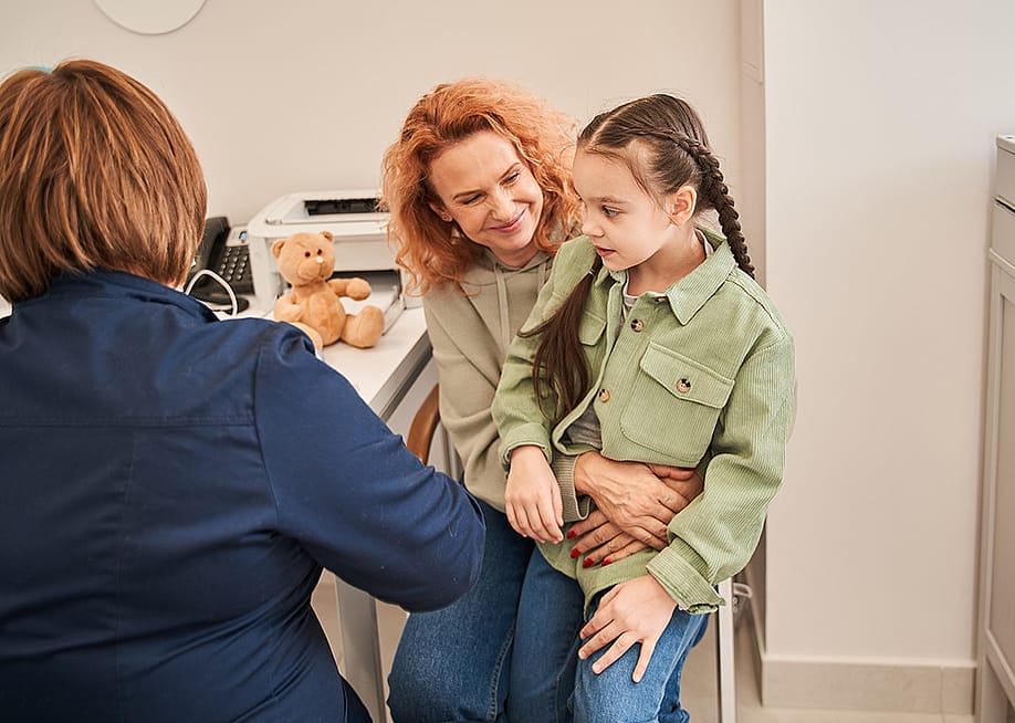 A little girl sitting on her parent's lap during a doctor's consultation. — Olena Yakobchuk // Shutterstock