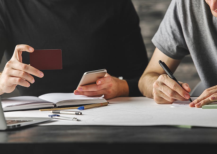 Young man holding credit card beside another person writing down information. — Peshkova // Shutterstock