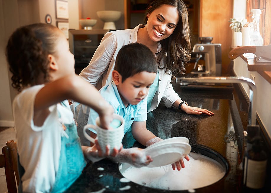 A mother with her two children washing dishes in the kitchen. — PeopleImages // Shutterstock