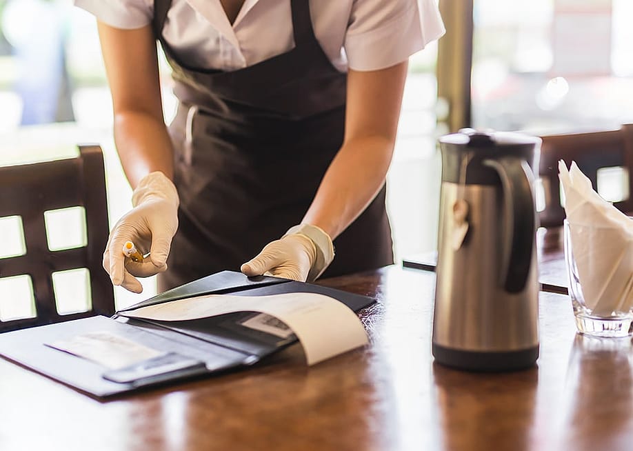 A restaurant waiter collecting the bill from a customer's table. — Bignai // Shutterstock