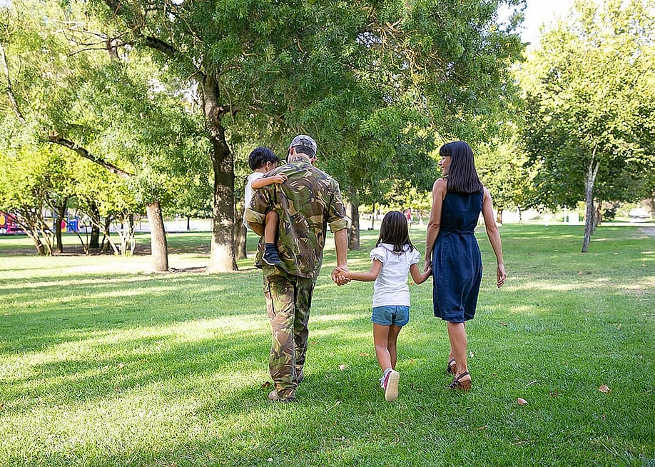 Back view of happy family walking together in a park. The father is wearing camouflage military uniform. — Mangostar // Shutterstock