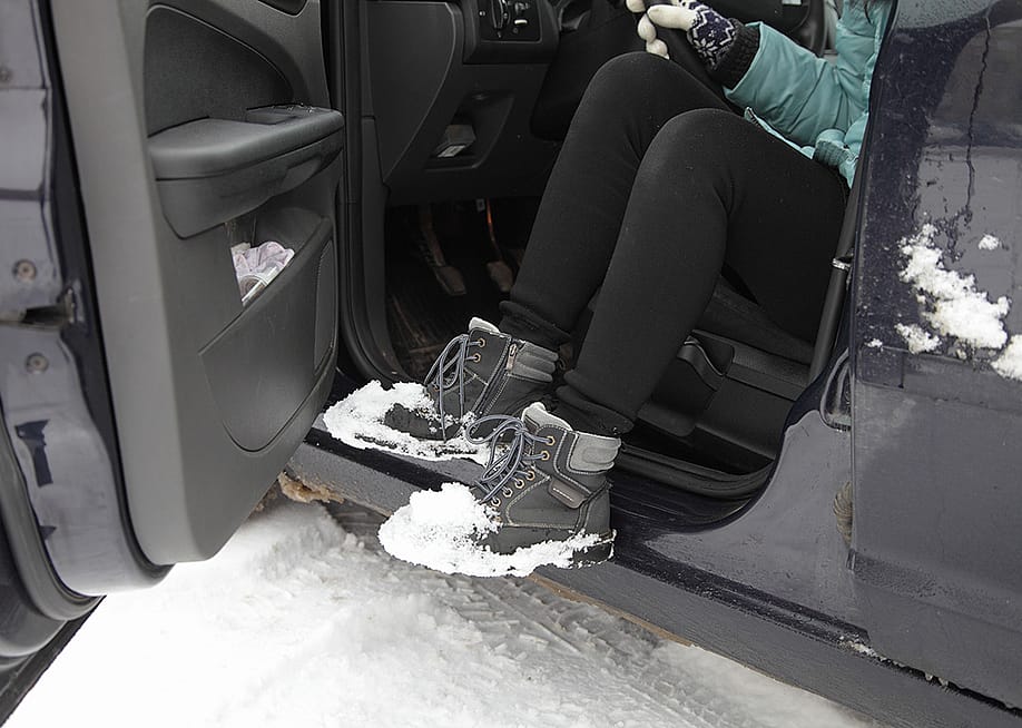 A young woman shaking snow off her boots while getting out of a car. — ilmarinfoto // Shutterstock