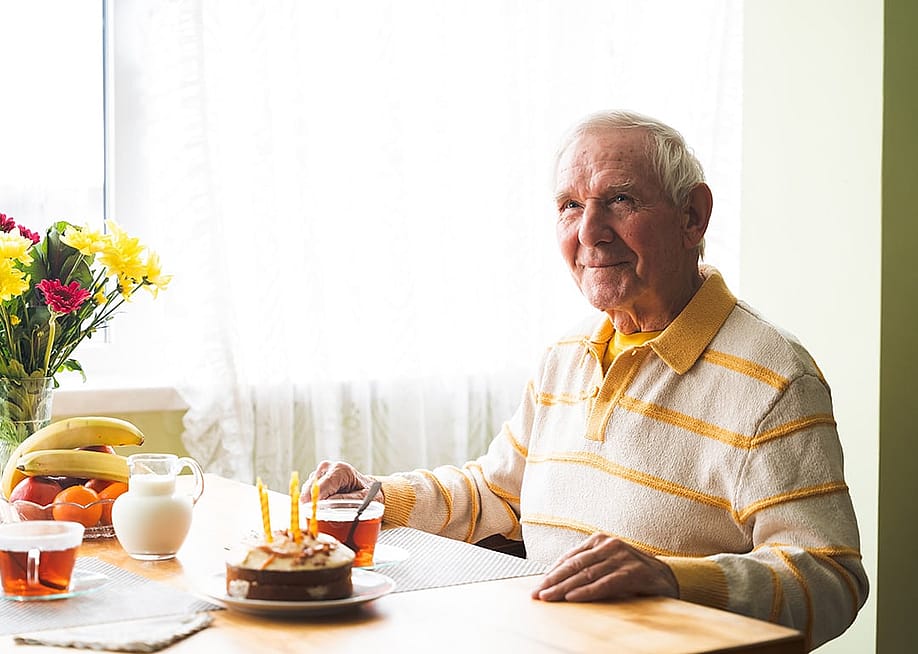 A happy senior old man seated by a dining table with cake. — Olena Yakobchuk // Shutterstock