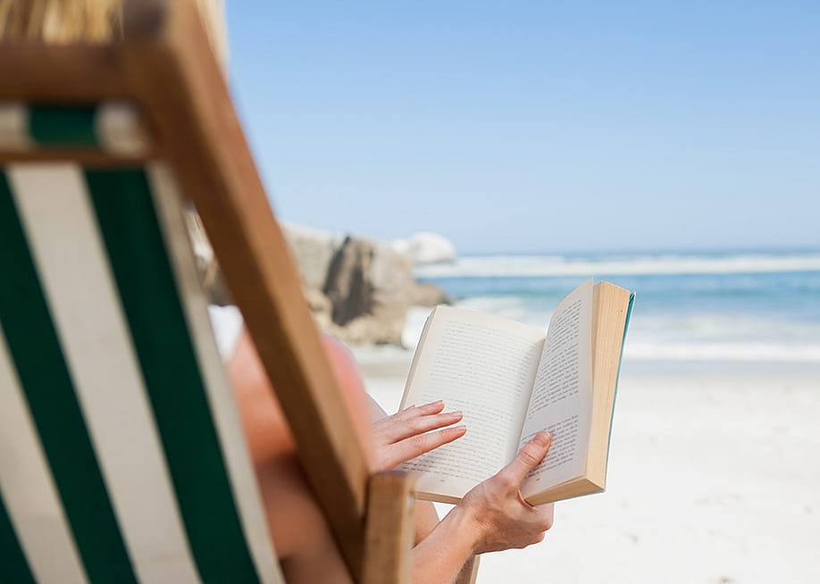 A woman reading a book at the beach. — wavebreakmedia // Shutterstock