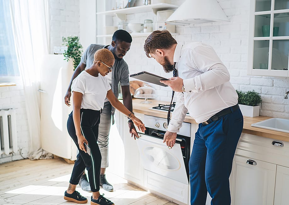 Three people inspecting an oven together in a kitchen area. — GaudiLab // Shutterstock