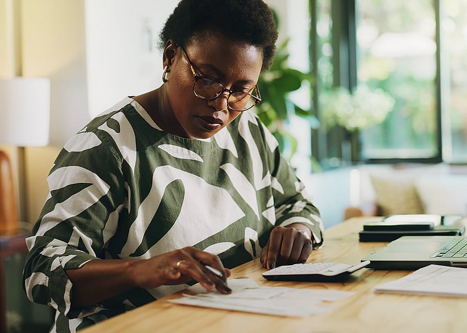 A black woman reviewing and calculating financial reports at home. — PeopleImages // Shutterstock