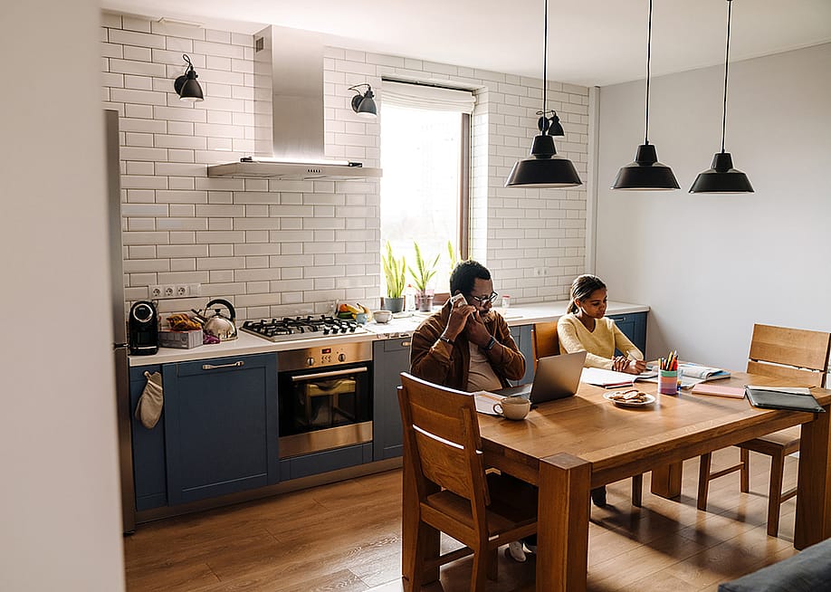 A father talking on the phone while his daughter does homework at home. — Dean Drobot // Shutterstock