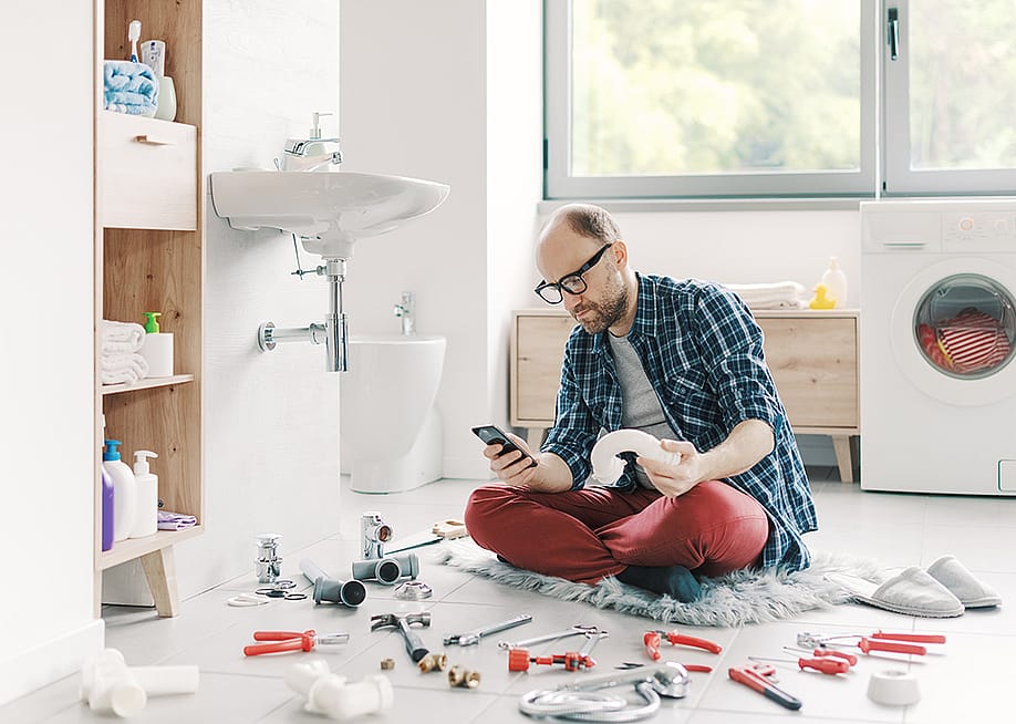 A man watching something on his smartphone while repairing a sink at home. — Stock-Asso // Shutterstock