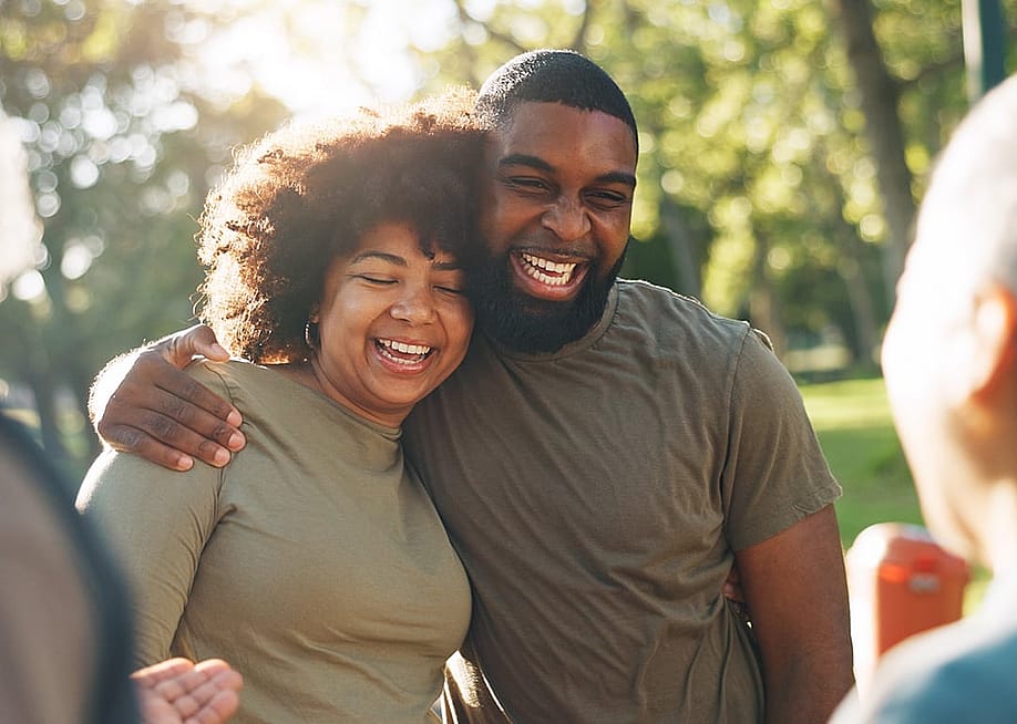 A happy Black couple hug and laugh outdoors. — PeopleImages // Shutterstock
