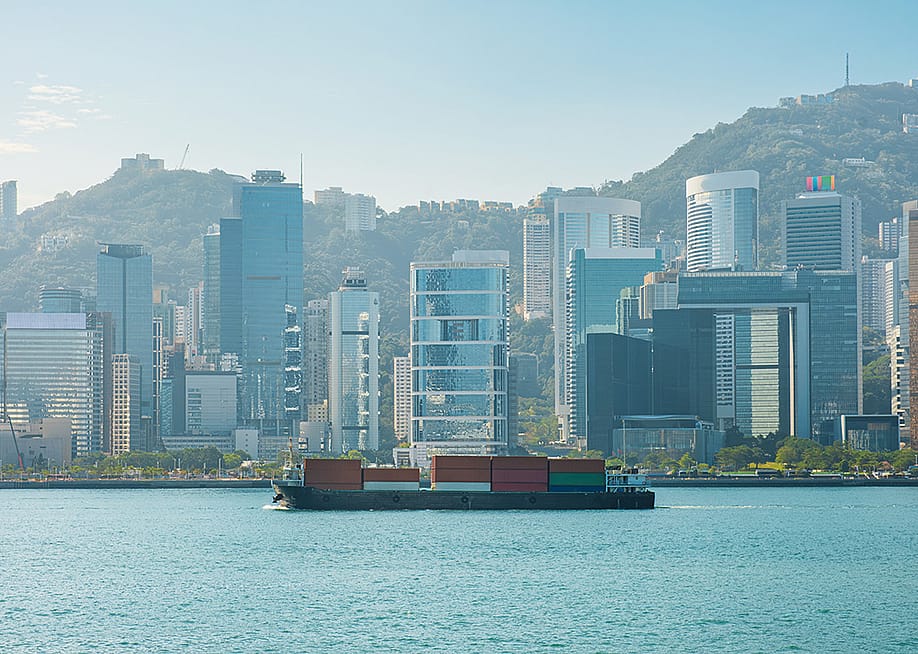 A cargo ship on the Victoria Harbour with the Hong Kong skyline in the background. — artem evdokimov // Shutterstock