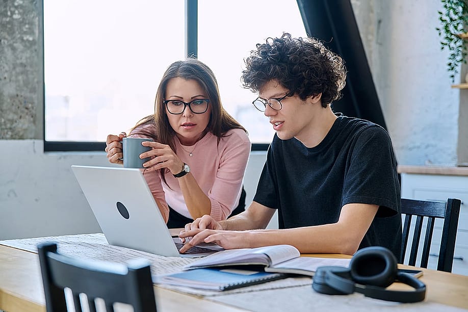A mother and her Gen Z son looking at a laptop together at home. — VH-studio // Shutterstock