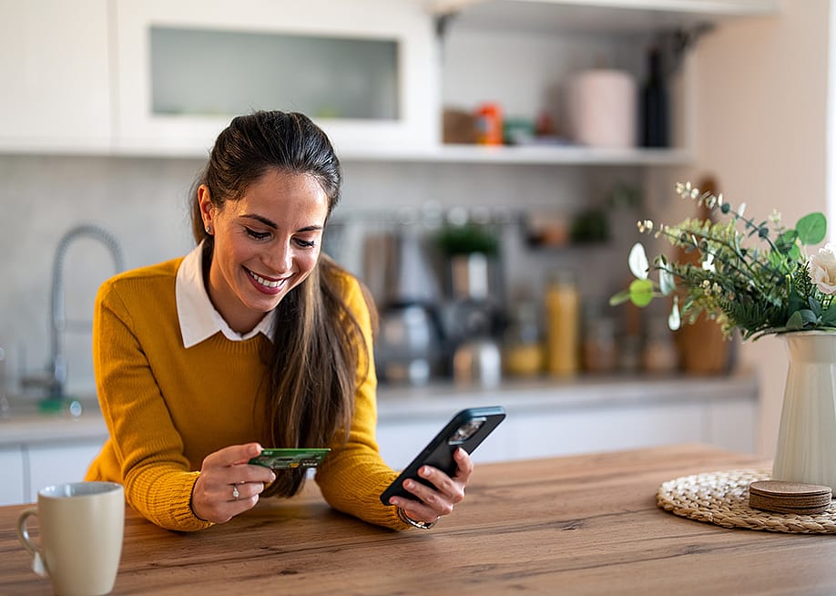 A woman using a smartphone, holding a credit card, while also checking an online bank account. — Dorde Krstic // Shutterstock