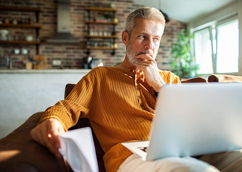 A man thinking with a laptop on his lap at home. — Geber86 // Shutterstock