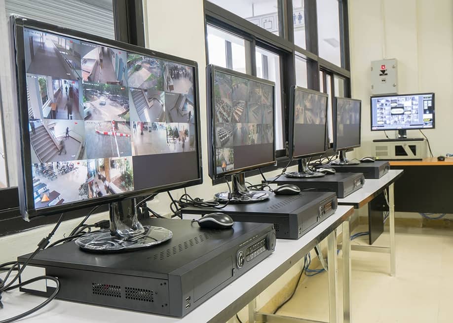 A security room with a row of monitors displaying multiple CCTV footage areas. — xfilephotos // Shutterstock