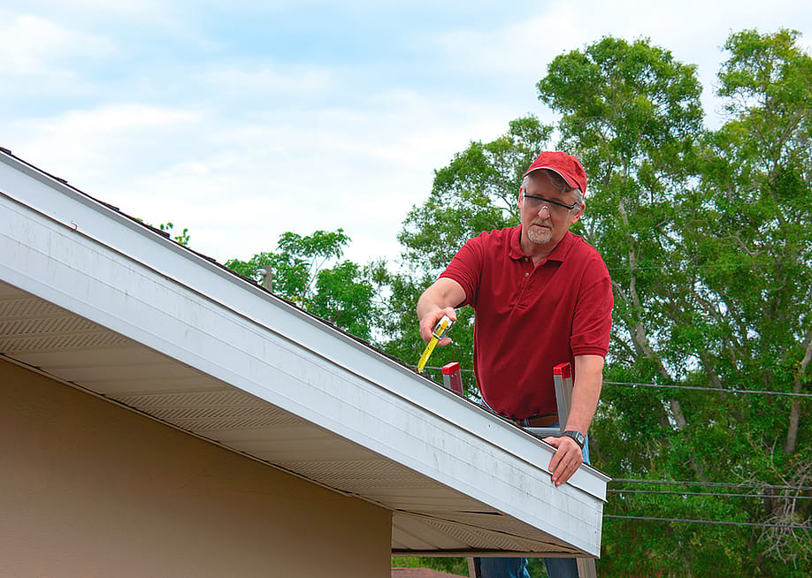 A wind mitigation inspector on a ladder doing inspection on a homeowner's new roof. — Michael O'Keene // Shutterstock