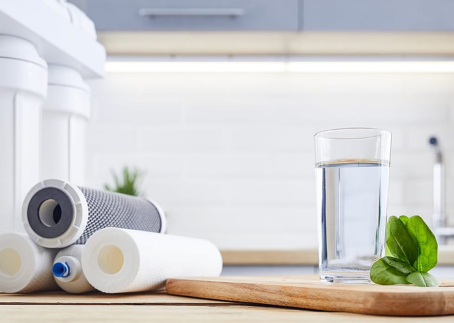 A glass of clean filtered water beside replacement filters of an osmosis water filtration system. — wertinio // Shutterstock