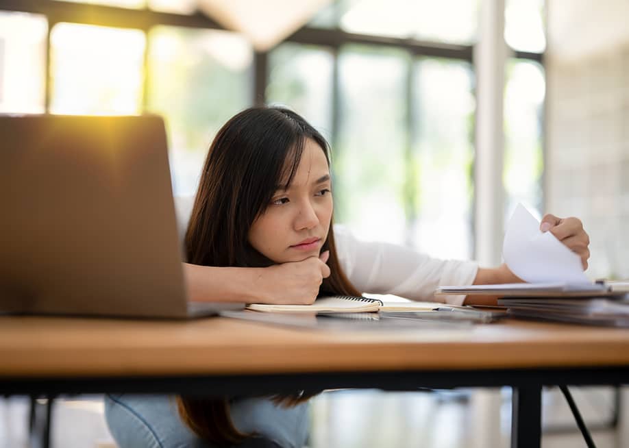 A tired employee looking though a paperwork in the office. — Wasana Kunpol // Shutterstock