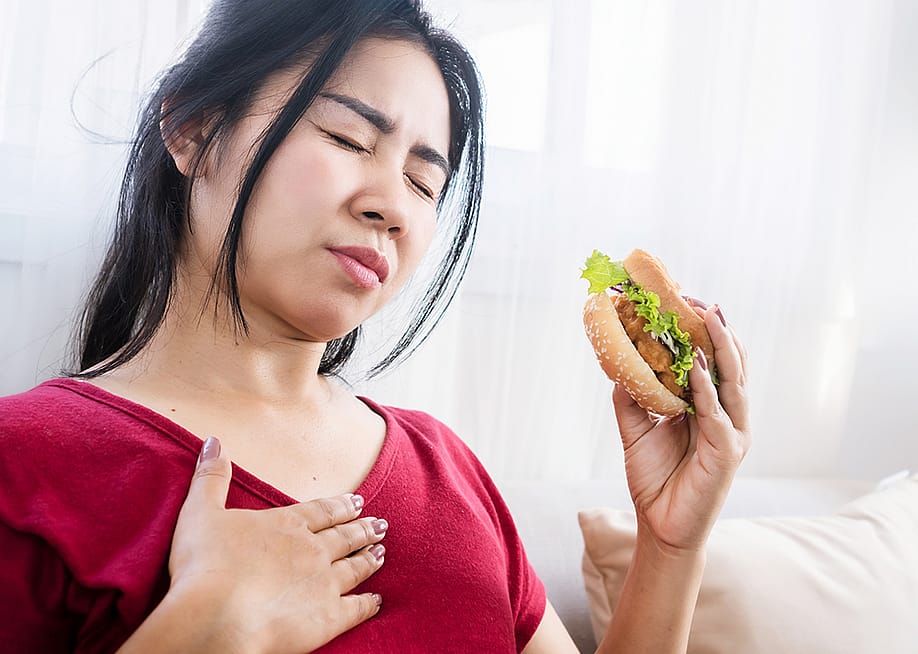 A person experiencing a heartburn while eating a burger. — Doucefleur // Shutterstock