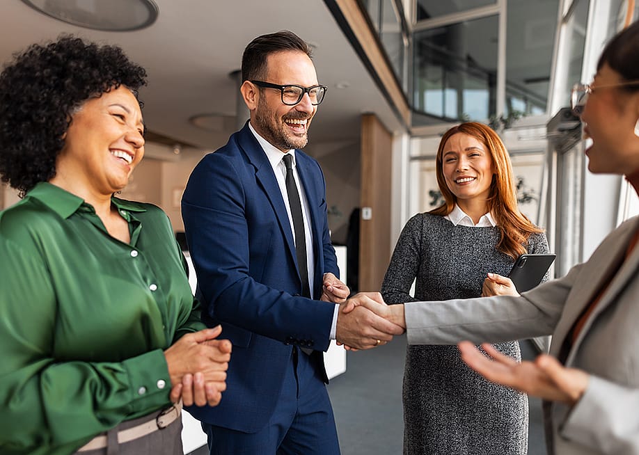 Coworkers engaging each other with handshakes in an office. — Jelena Zelen // Shutterstock