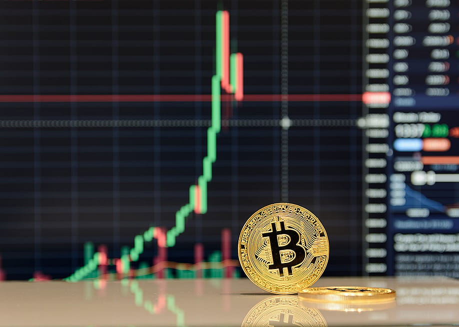 A golden bitcoin in front of stock exchange charts. — fotobubas // Shutterstock