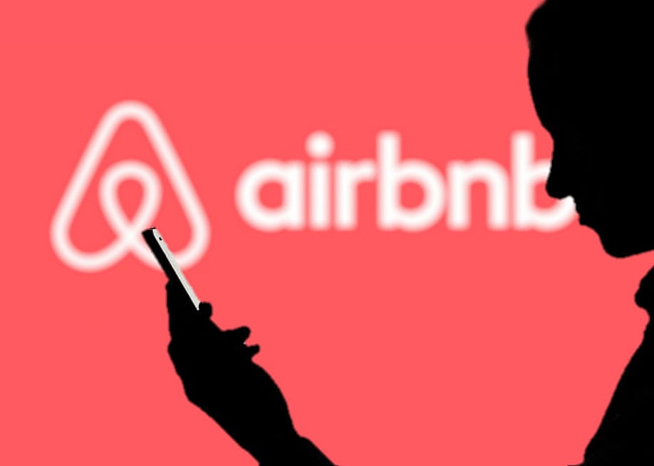 Silhouette of a man using a phone against a background showing Airbnb's logo. — Poetra.RH // Shutterstock